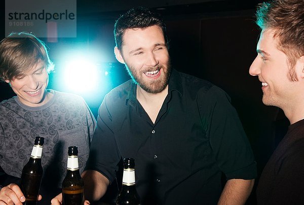 Drei männliche Freunde trinken Flaschenbier im Nachtclub.