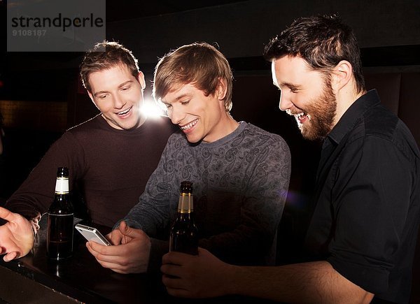 Drei männliche Freunde suchen Smartphone im Nachtclub