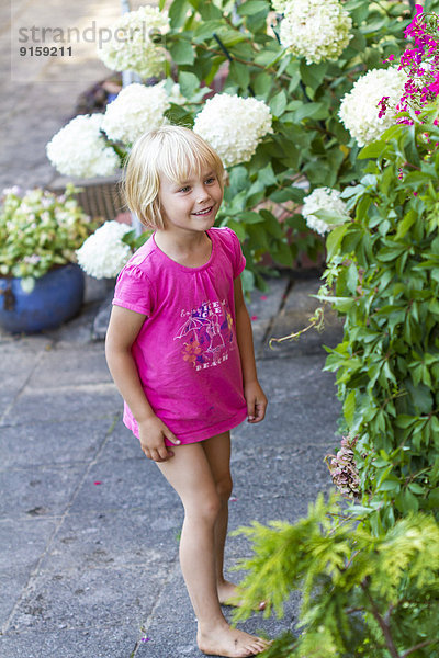 Lächelndes Mädchen schaut sich Blumen imGarten an