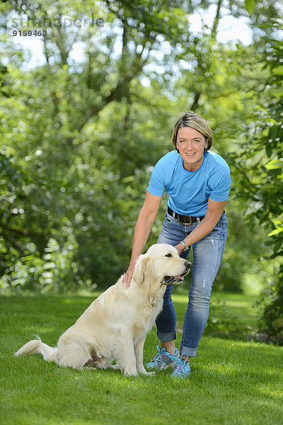 Reife Frau mit einem Golden Retriever im Garten