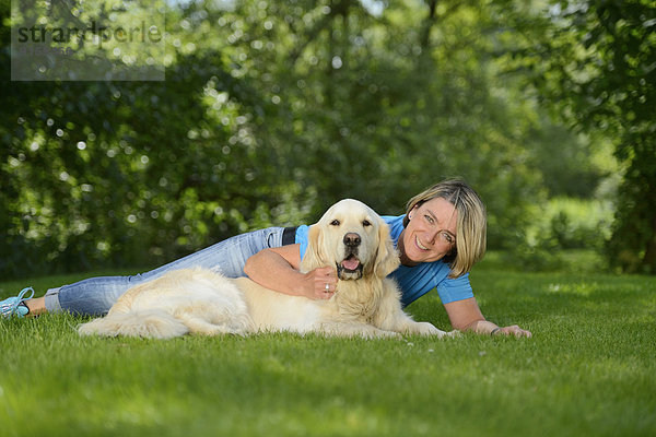 Reife Frau mit einem Golden Retriever im Garten