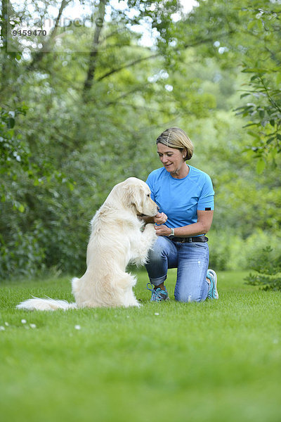 Reife Frau mit einem Golden Retriever im Garten