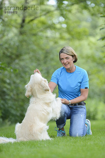 Reife Frau mit einem Golden Retriever im Garten