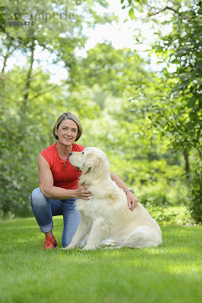 Reife Frau mit einem Golden Retriever im Garten