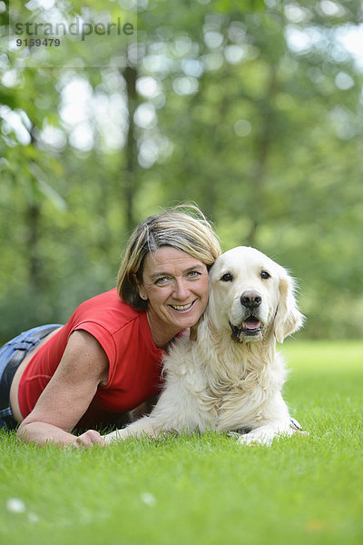 Reife Frau mit einem Golden Retriever im Garten