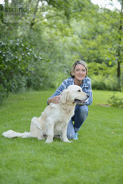 Reife Frau mit einem Golden Retriever im Garten