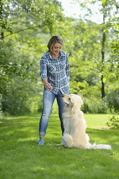 Reife Frau mit einem Golden Retriever im Garten