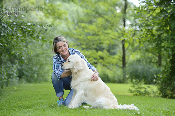 Reife Frau mit einem Golden Retriever im Garten