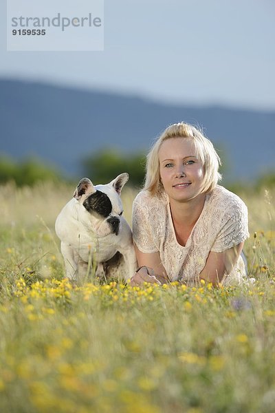 Frau liegt auf einer Wiese mit einer sieben Monate alten Französischen Bulldogge