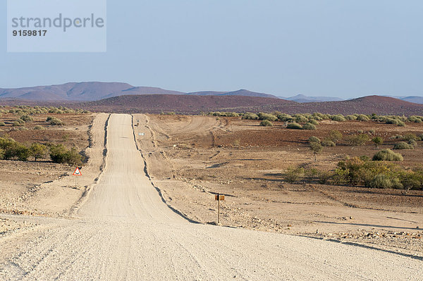 Weite  gerade Schotterstraße in Trockenlandschaft  Kunene Region  Namibia