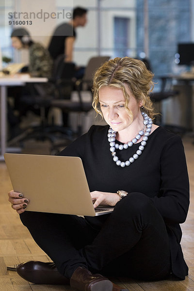 Volle Länge der reifen Geschäftsfrau mit Laptop  während sie im Büro auf dem Boden sitzt.