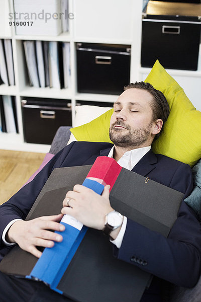 Mittlerer erwachsener Geschäftsmann mit Ordner auf Sofa im Büro