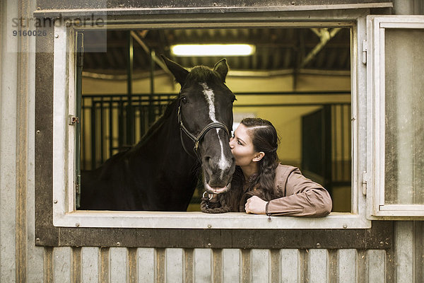 Junge Frau küsst Pferd im Stall