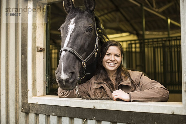 Porträt einer glücklichen jungen Frau mit Pferd im Stall