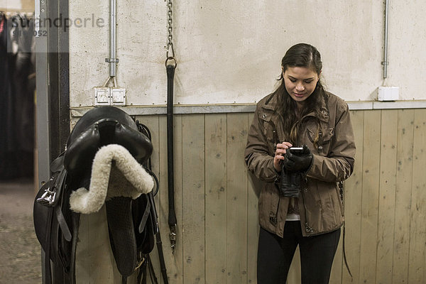 Junge Frau mit Smartphone im Pferdestall