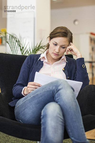 Mittlere erwachsene Geschäftsfrau beim Lesen von Dokumenten im Büro