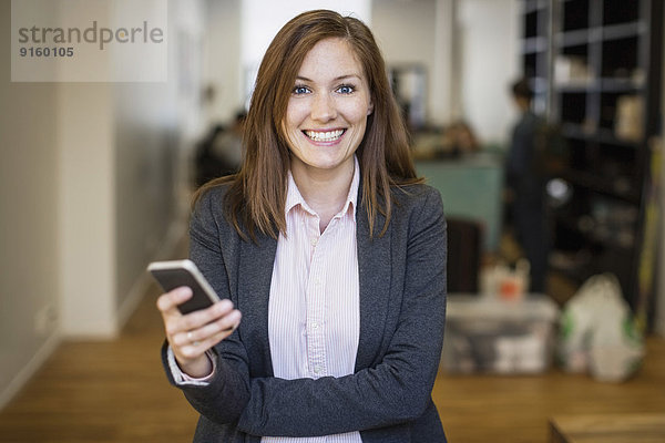 Porträt einer lächelnden Geschäftsfrau mit Handy im Büro
