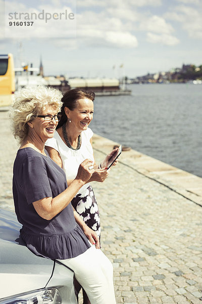 Glückliche Seniorinnen  die sich am Flussufer an das Auto lehnen