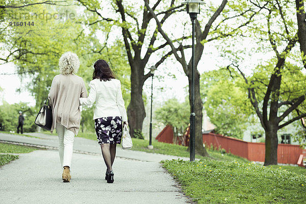 Rückansicht älterer Freundinnen beim Spaziergang am Gartenweg