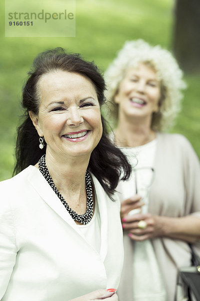 Porträt einer glücklichen Seniorin im Park mit einer im Hintergrund stehenden Freundin