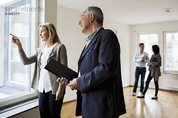 Immobilienmakler diskutieren  während ein Paar im Hintergrund bei einem neuen Zuhause steht