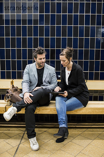Volle Länge der Geschäftsleute  die über digitale Tabletten diskutieren  während sie auf einer Bank in der U-Bahn-Station sitzen.