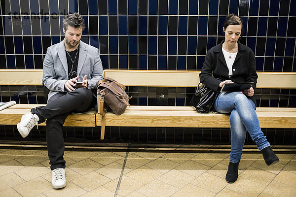 Volle Länge der Personen  die Technologien auf der Bank in der U-Bahn-Station benutzen.