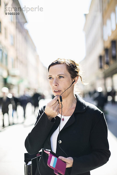 Reife Geschäftsfrau  die über Kopfhörer auf der Straße spricht