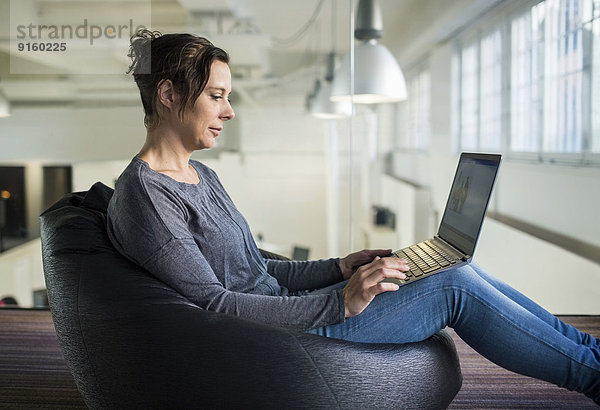 Seitenansicht einer reifen Geschäftsfrau  die im Büro auf einem Laptop sitzt.
