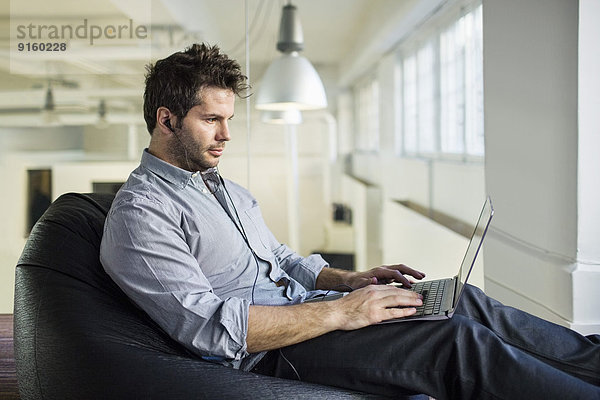 Mittlerer erwachsener Geschäftsmann mit Laptop  während er im Büro auf einer Bohnentüte sitzt.