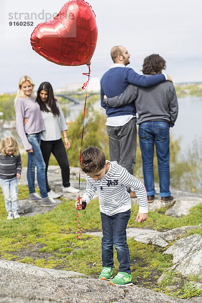 Junge hält Ballon auf Felsen mit homosexuellen Familien im Hintergrund