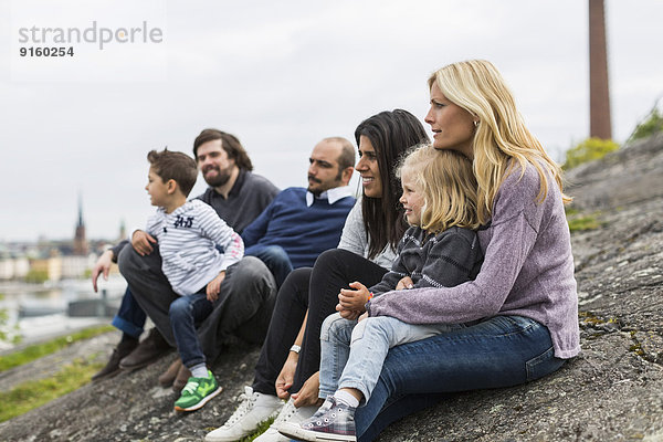 Homosexuelle Familien entspannen sich auf dem Felsen am Seeufer