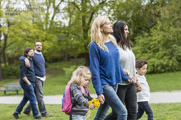 Weibliche homosexuelle Familie beim Spaziergang im Park mit schwulem Paar im Hintergrund