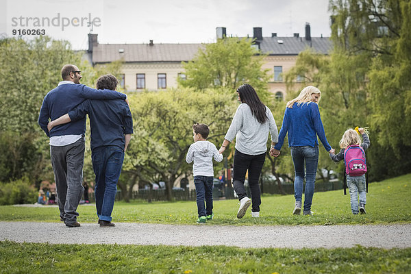 Rückansicht der weiblichen homosexuellen Familie beim Spaziergang im Park mit schwulem Paar im Hintergrund
