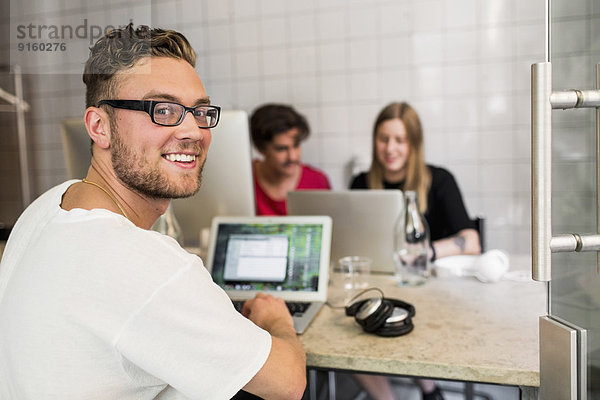 Porträt eines glücklichen jungen Geschäftsmannes mit Kollegen im Hintergrund im Kreativbüro