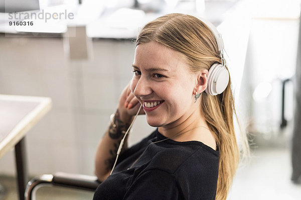 Lächelnde junge Geschäftsfrau mit Kopfhörer im Kreativbüro