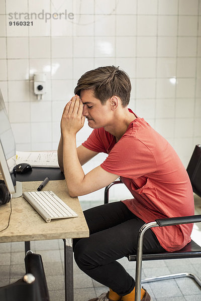 Besorgter junger Geschäftsmann mit umklammerten Händen sitzt am Computertisch im neuen Büro