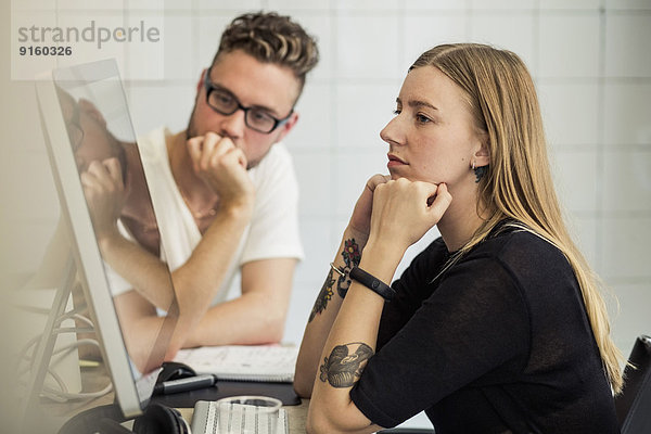 Junger Geschäftsmann und Geschäftsfrau beim Blick auf den Computermonitor im Kreativbüro