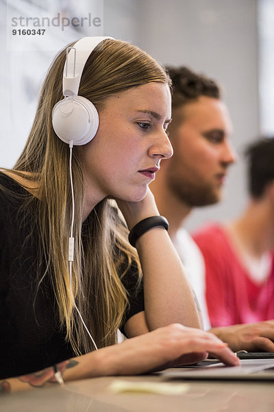 Junge Geschäftsfrau hört Kopfhörer  während sie den Laptop im neuen Büro benutzt.