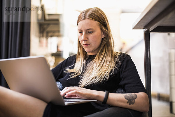 Junge Geschäftsfrau  die im kleinen Büro auf einem Laptop sitzt.