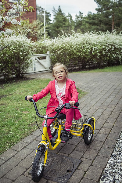 Porträt eines Mädchens mit Down-Syndrom beim Fahrradfahren im Rasen