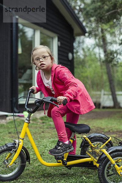 Porträt eines Mädchens mit Down-Syndrom beim Fahrradfahren im Rasen