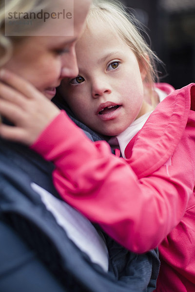 Mädchen mit Down-Syndrom von der Mutter getragen