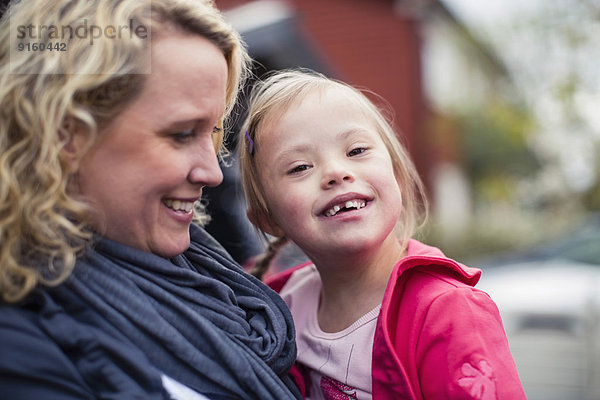 Porträt eines glücklichen Mädchens mit Down-Syndrom  getragen von der Mutter