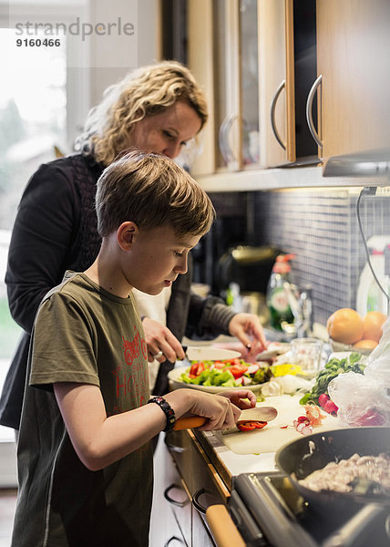 Sohn und Mutter schneiden Gemüse in der Küche