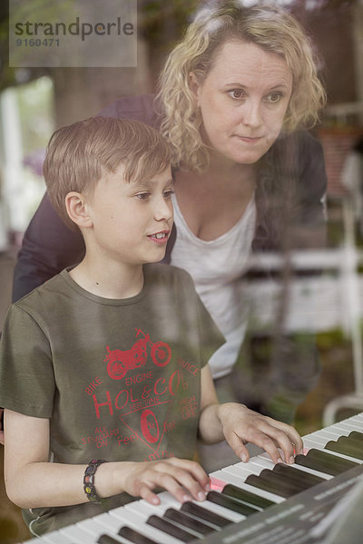 Mutter unterrichtet Klavier an Sohn im Haus