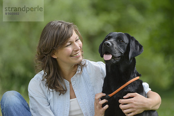 Frau mit einem schwarzen Labrador auf einer Wiese  Bayern  Deutschland  Europa