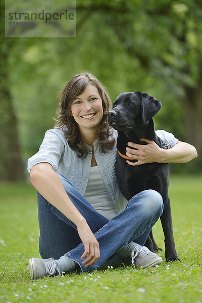 Frau mit einem schwarzen Labrador auf einer Wiese  Bayern  Deutschland  Europa