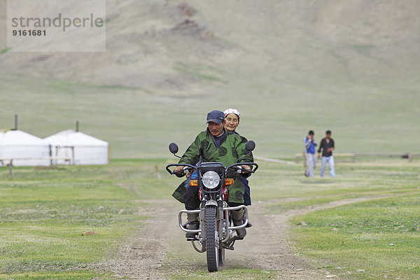 Ehepaar im traditionellen Deel fährt auf einem Motorrad  Terkhiyn Tsagaan Nuur  Nordsteppe  Archangai-Aimag  Mongolei