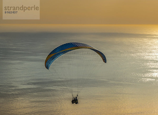 Paraglider-Tandemsprung  Gleitschirm fliegt über dem Meer bei Sonnenuntergang  Kapstadt  Westkap  Republik Südafrika